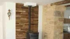Una habitación con piso de madera, una mesa con un cuenco blanco, una chimenea y una pared de piedra.