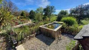 Un jardín con un estanque, diversas plantas y una cerca de madera.