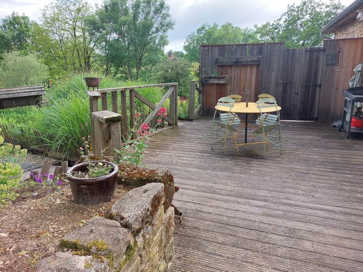 Un espace extérieur rustique agrémenté d’une terrasse en bois, d’une table rustique avec des chaises et d’une clôture en bois.