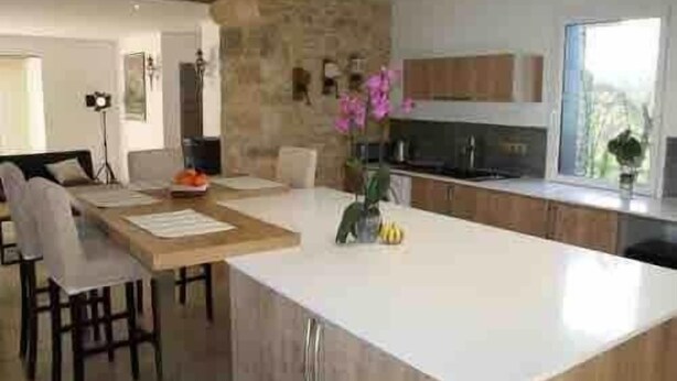 Una cocina moderna con una isla central, un comedor con sillas y una pared de acento de piedra.