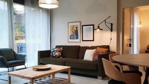 Una sala de estar con un sofá, una mesa de centro y una mesa de comedor. Hay dos cuadros en la pared.
