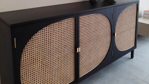Un mueble negro con tres grandes puertas circulares, una obra de arte enmarcada encima y un florero verde en la parte superior.