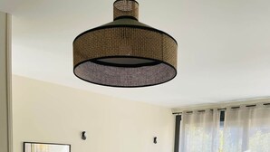 Un comedor moderno con una mesa redonda, sillas, una lámpara colgante, un mueble con paneles decorativos, un televisor y una ventana con cortinas.