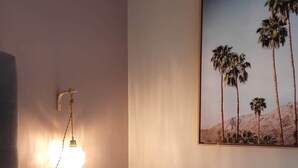 Un dormitorio con una cama, una lámpara fijada a la pared y un cuadro con palmeras.
