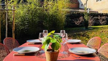 An outdoor dining area with round tables and chairs, a potted plant, and a view of a building in the background.