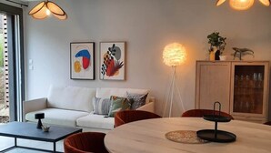 A modern living room with a white sofa, red chairs, a round dining table, and two pendant lights. - Le Spicy 2 minutes historical center parking (Sarlat-la-Canéda)