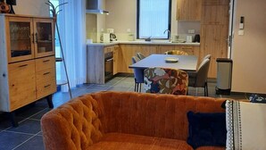 A modern kitchen with wooden cabinets, a dining table, and a sofa in the living area.