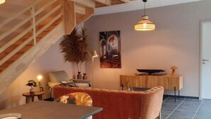 A modern living room with a wooden staircase, a sofa, a dining table, and a pendant light.