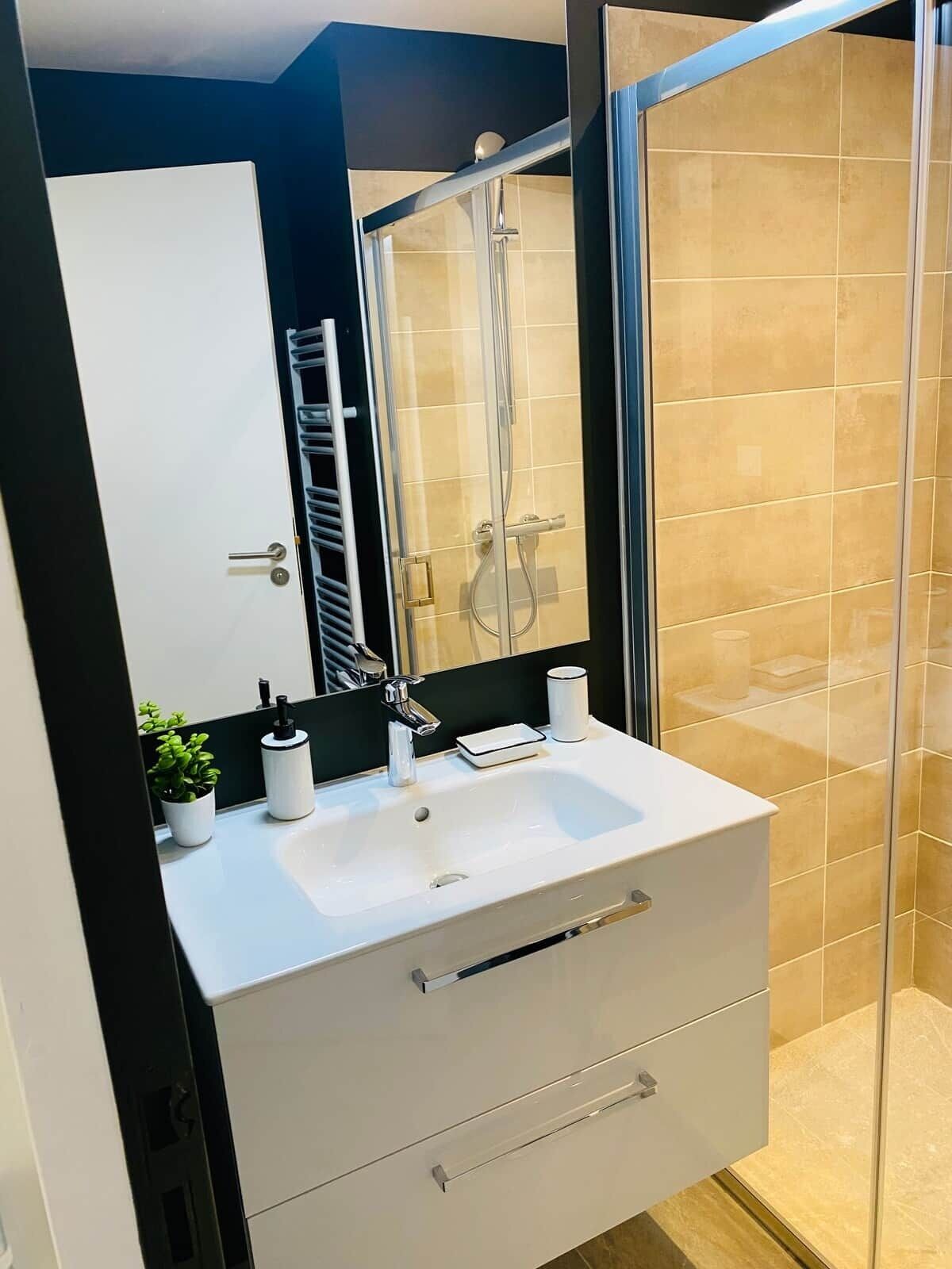 Un baño moderno con tocador blanco, cabina de ducha de vidrio y un espejo grande.