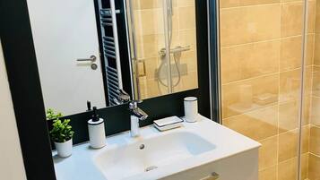 Un baño moderno con tocador blanco, cabina de ducha de vidrio y un espejo grande.
