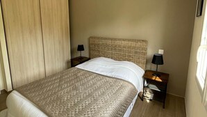 A bedroom with a bed, a woven headboard, two bedside tables with lamps, and a hanging light fixture. - House sleeps 6 pool (Sarlat-la-Canéda)