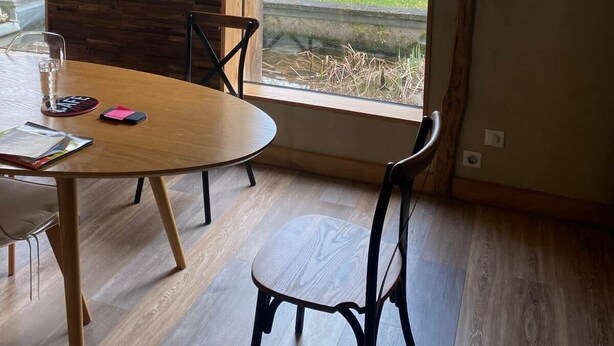 A modern dining area with a wooden table and chairs, a hanging light fixture, and a view of the outdoors through a large window. - Atypical pool house in a bucolic setting. (Campagnac-lès-Quercy)
