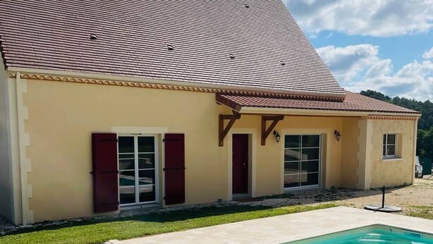 A house with a swimming pool, a tiled deck, and a red-tiled roof.