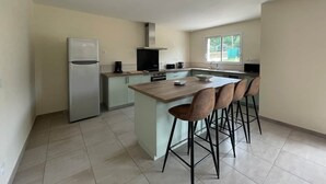 A modern kitchen with a central island, bar stools, a refrigerator, and a window providing natural light.