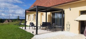 A covered outdoor seating area with chairs and a table, adjacent to a building with a red roof and beige walls. - Quiet house* Valley view* Near Sarlat (Saint-André-d'Allas)