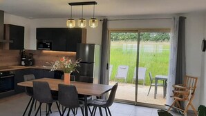 Een moderne keuken met donkere kastjes, een houten eettafel en uitzicht op een grasveld door grote schuifdeuren.