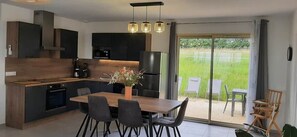 A modern kitchen with dark cabinetry, a wooden dining table, and a view of a grassy outdoor area through large sliding doors. - Quiet house* Valley view* Near Sarlat (Saint-André-d'Allas)