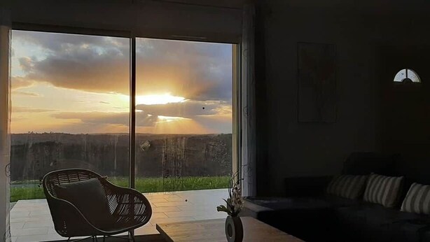 Een kamer met een grote schuifpui die uitkomt op een buitengebied. Binnenin staat een zwarte bank en een losse stoel.