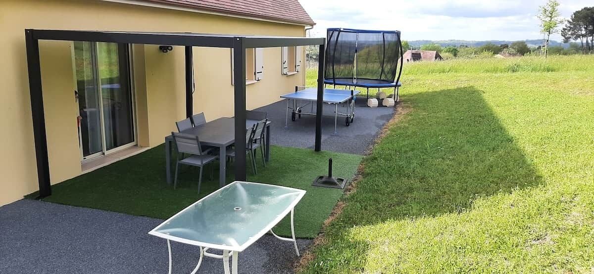 An outdoor patio with a table and chairs, a trampoline, and a covered seating area.