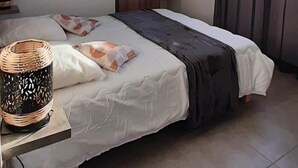 Een slaapkamer met een bed, een hanglamp, een plankenwand en een raam met gordijnen.