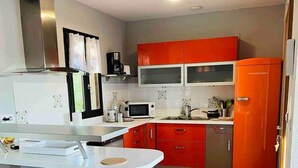A modern kitchen with a central island, red cabinets, and a stainless steel range hood. - Villa*Piscine*Proche Sarlat (Proissans)