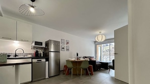 Una cocina compacta con electrodomésticos modernos, un comedor con mesa y sillas, y vistas al exterior a través de un amplio ventanal.