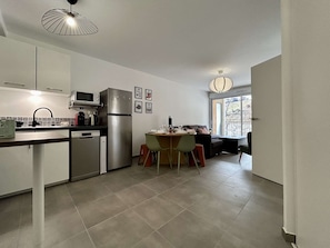A compact kitchen with modern appliances, a dining area with a table and chairs, and a view of the outdoors through a large window. - Modern apartment between city and cable car - 6 guests (Briançon)