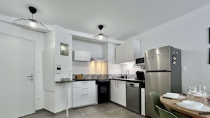 Una cocina moderna con armarios blancos, electrodomésticos de acero inoxidable y un comedor con mesa y sillas.