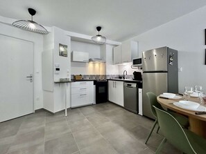 A modern kitchen with white cabinetry, stainless steel appliances, and a dining area with a table and chairs. - Modern apartment between city and cable car - 6 guests (Briançon)