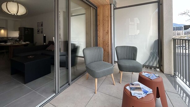 Una sala de estar moderna con un sofá, dos sillones, una mesita de centro y un balcón con barandilla.