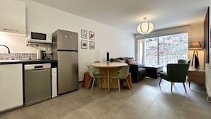 Cocina compacta equipada con microondas, refrigerador y lavavajillas. Cuenta con una zona de comedor con una mesa redonda y sillas, además de un sofá con vistas al exterior.