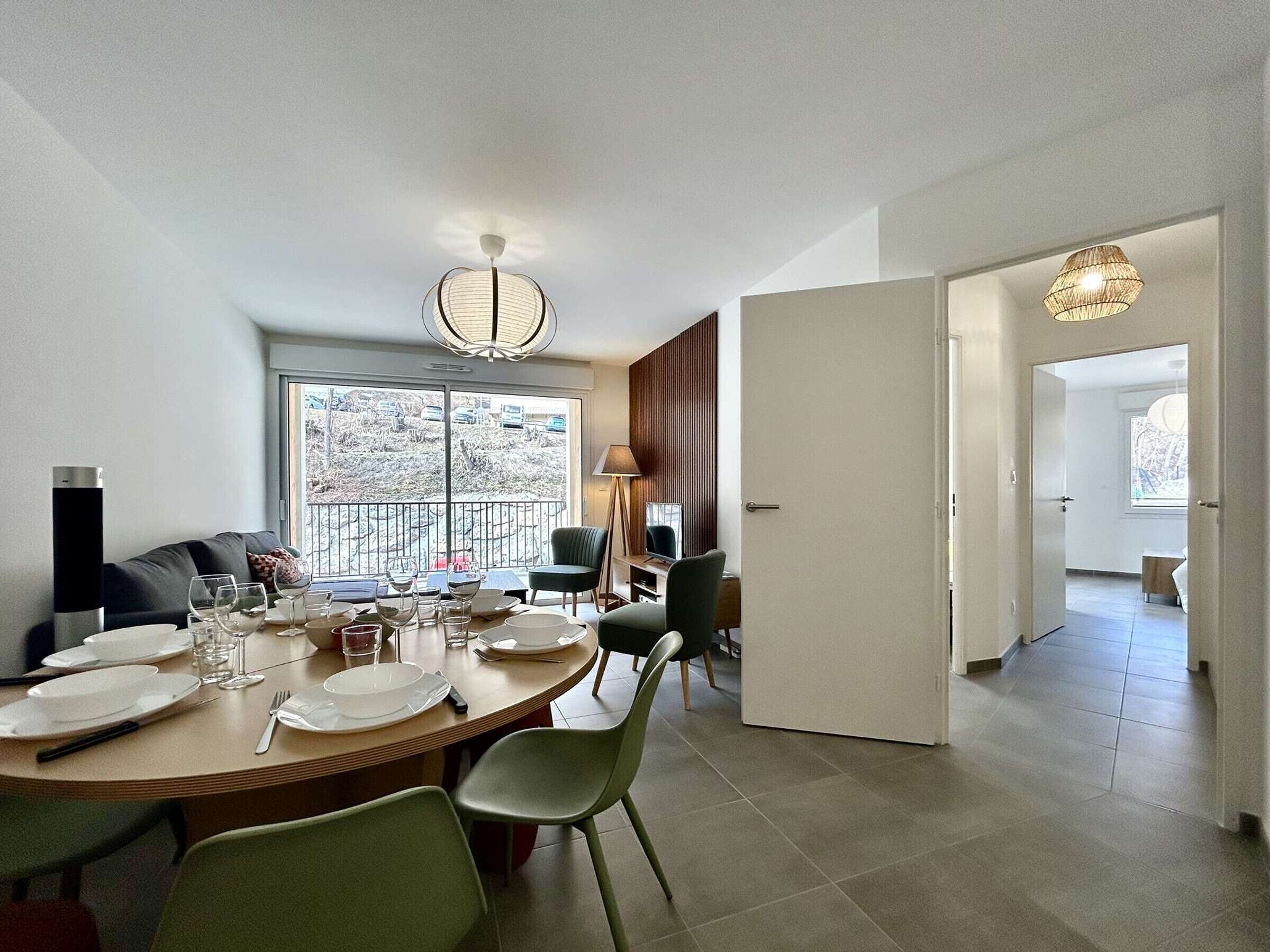 A modern dining area with a round table set for four, a sofa, and a view of a snowy landscape through large windows.