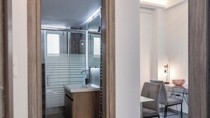 A modern kitchen with a built-in oven, a sink, and a dining area with a table and chairs. - Daedalus Minimal 1bedroom Bliss (Athina)