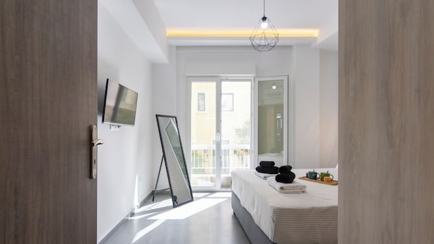 A modern hotel room with a bed, a flat-screen TV, a large window, and a door. - Daedalus Minimal 1bedroom Bliss (Athina)