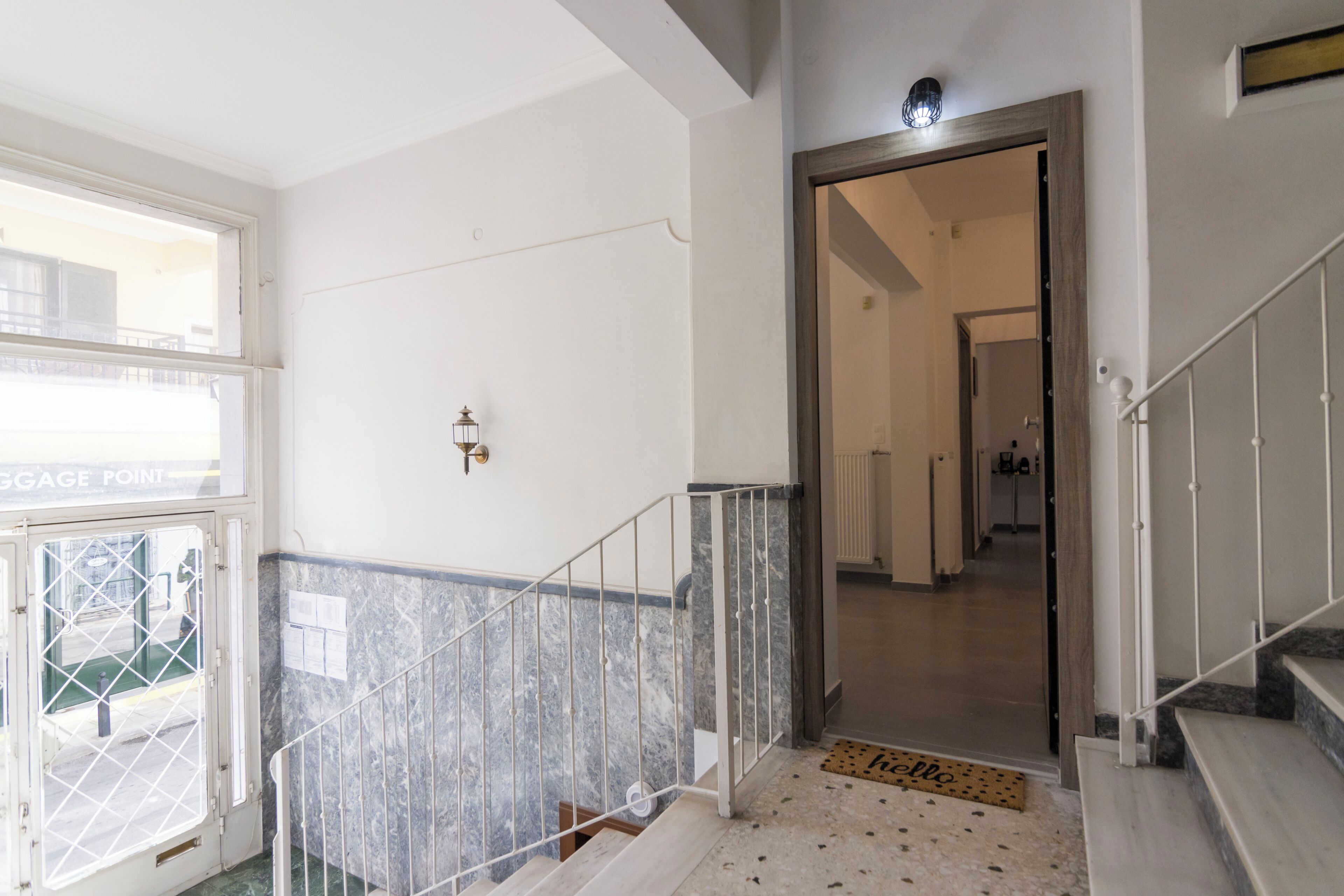 Un couloir avec un escalier en marbre, une porte dotée d’un portail en métal et un luminaire au plafond.