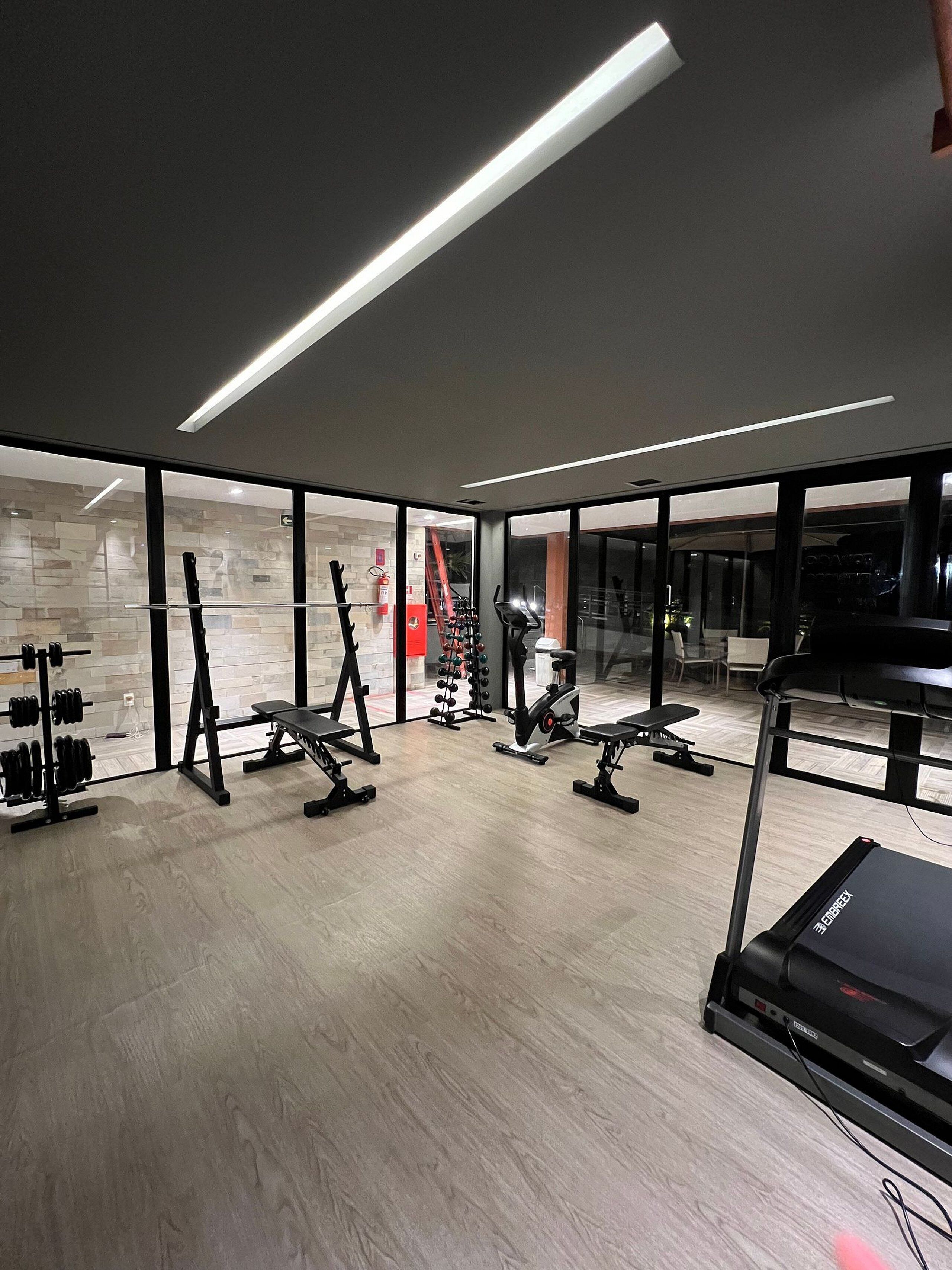 Une salle de sport moderne équipée de divers appareils d’exercice, dotée de grandes fenêtres et d’un plancher en bois.