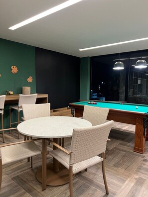 A pool table in a room with a green wall and a wooden floor. There are four chairs around the table.