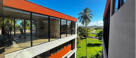 A modern building with large windows and a balcony overlooking a green landscape with palm trees.