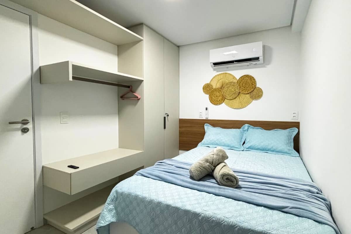 A bedroom with a bed, a wardrobe, a wall-mounted air conditioner, and a decorative wall piece.