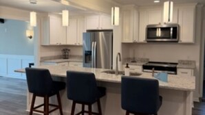 Una cucina moderna con mobili bianchi, elettrodomestici in acciaio inossidabile e un angolo bar con tre sgabelli.