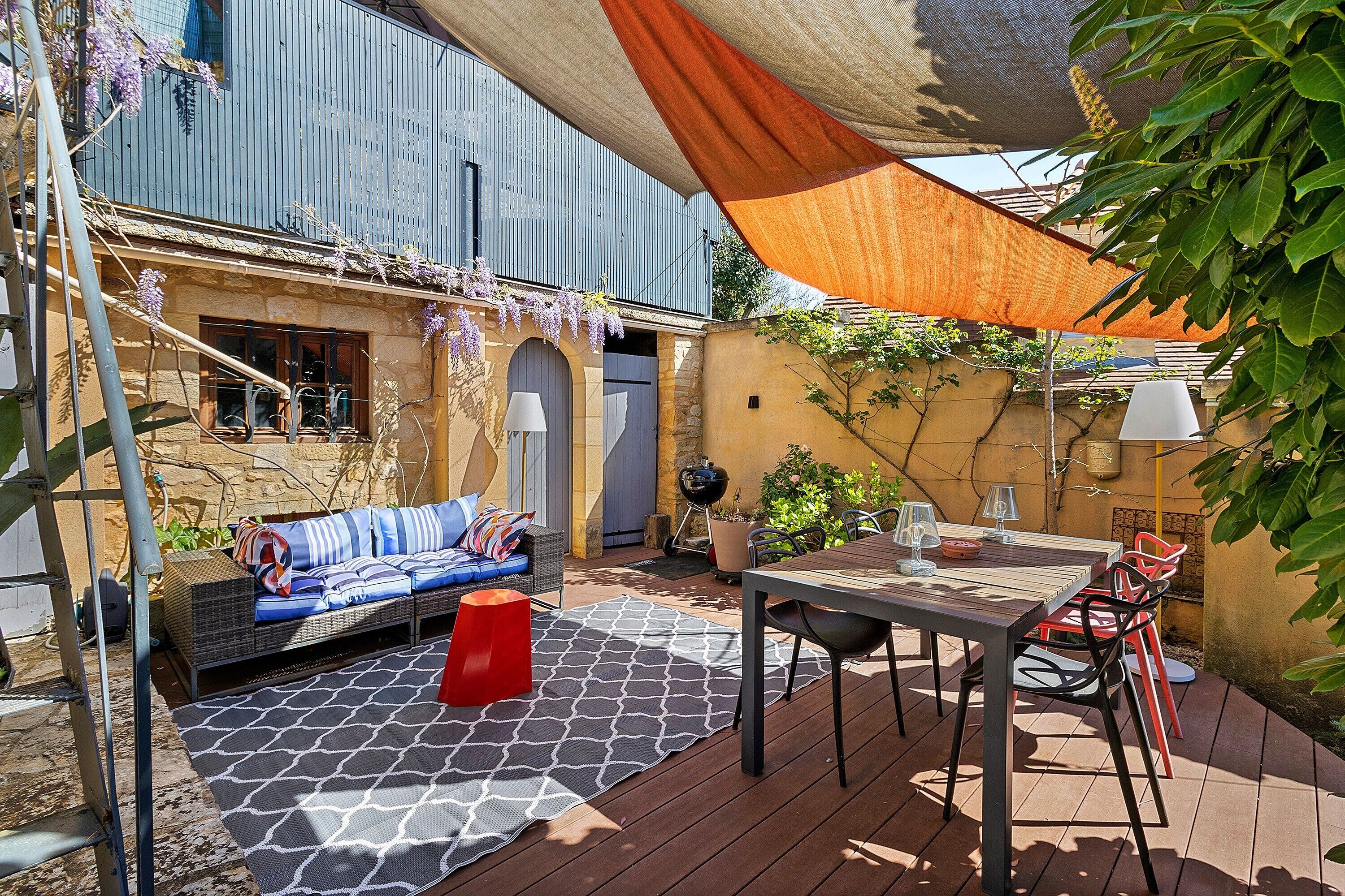 Eine Außenpatio mit einer Couch, einem Tisch, Stühlen, einer Pergola und einer Wand mit Kletterpflanzen.