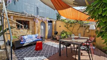 Eine Außenpatio mit einer Couch, einem Tisch, Stühlen, einer Pergola und einer Wand mit Kletterpflanzen.