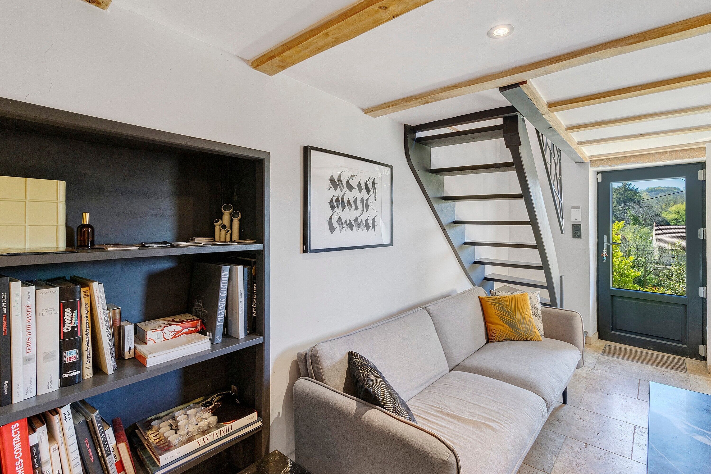 Una sala de estar moderna con un sofá, estanterías, una obra de arte enmarcada y una escalera.