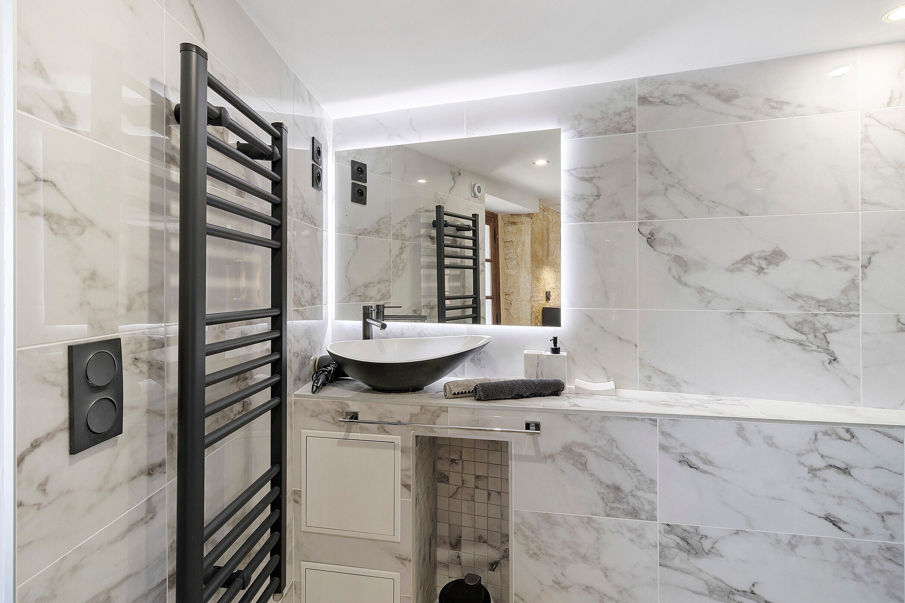 Une salle de bain moderne avec un porte-serviettes noir, un lavabo sur colonne et un grand miroir.