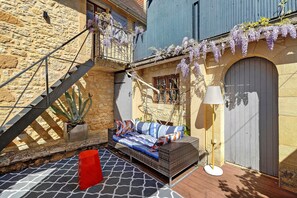 A stone building with a wrought iron staircase, a cushioned outdoor seating area, and a door with a decorative arch. - L'Annexe Premium Cottage, Périgord Noir (Groléjac)