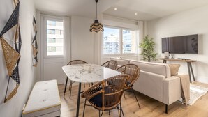 Een moderne woonkamer met een marmeren tafel, rieten stoelen, een bank en een tv op een houten standaard.