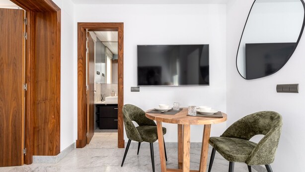 Zona pranzo moderna con tavolo rotondo in legno, due sedie imbottite, un televisore a schermo piatto e un grande specchio a parete.