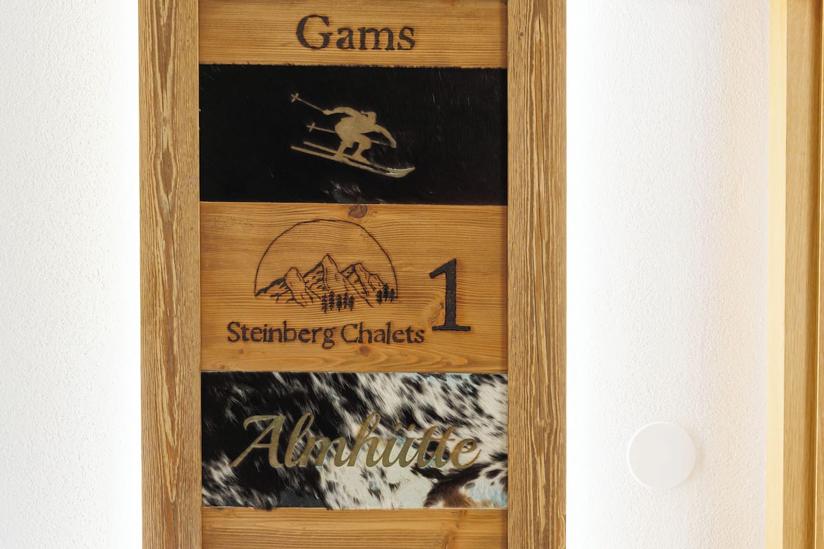 Uma placa de madeira com o texto 'Gams Steinberg Chalets 1 Alpenrose' em uma parede branca.
