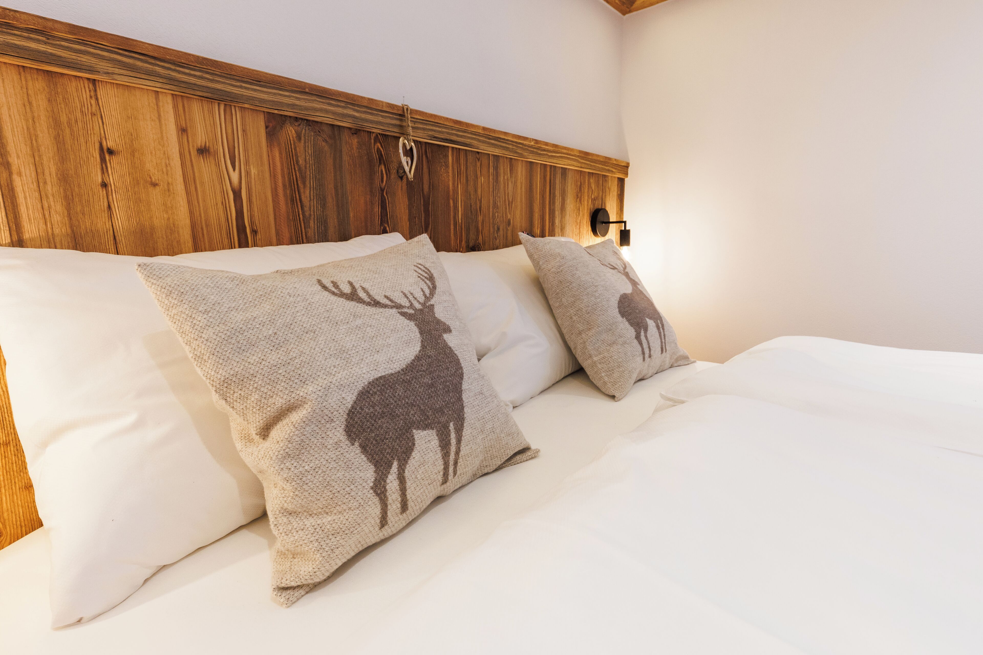 A bed with two pillows featuring a deer design, a wooden headboard, and a wall-mounted light fixture.