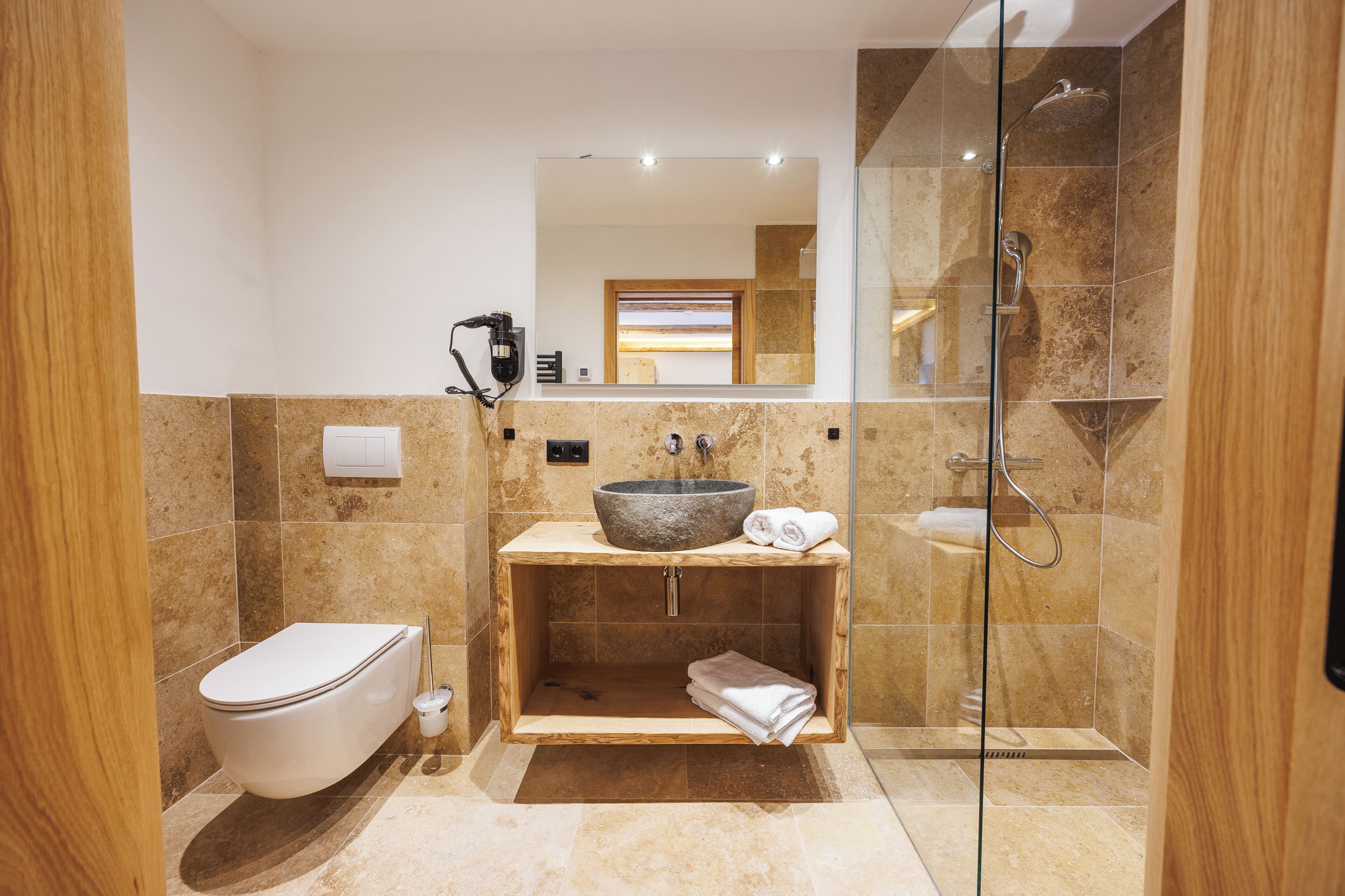 Un baño moderno con inodoro, un lavamanos grande, ducha con mampara de vidrio y tocador de madera.